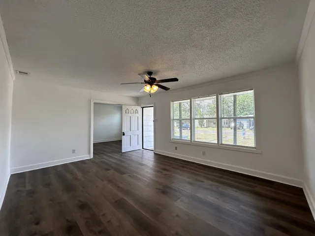an empty room with wooden floor chandelier fan and windows