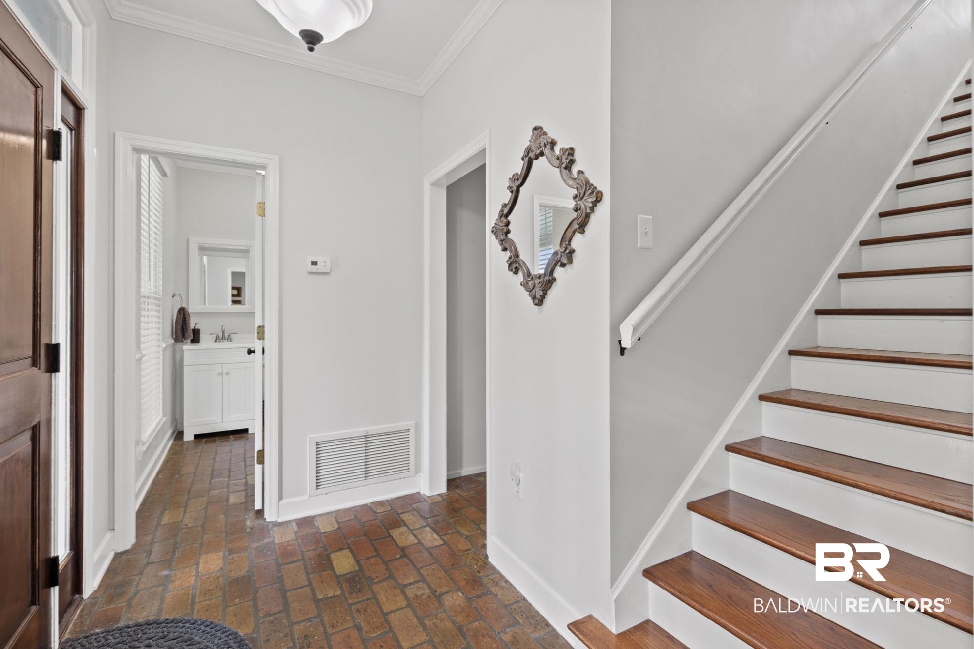 12171 Marguerite Drive Coden, AL 36523 - Photo 7 of 44 Entryway featuring brick flooring, a hardwood staircase with white risers, and a white vanity with a rectangular sink in the visible room