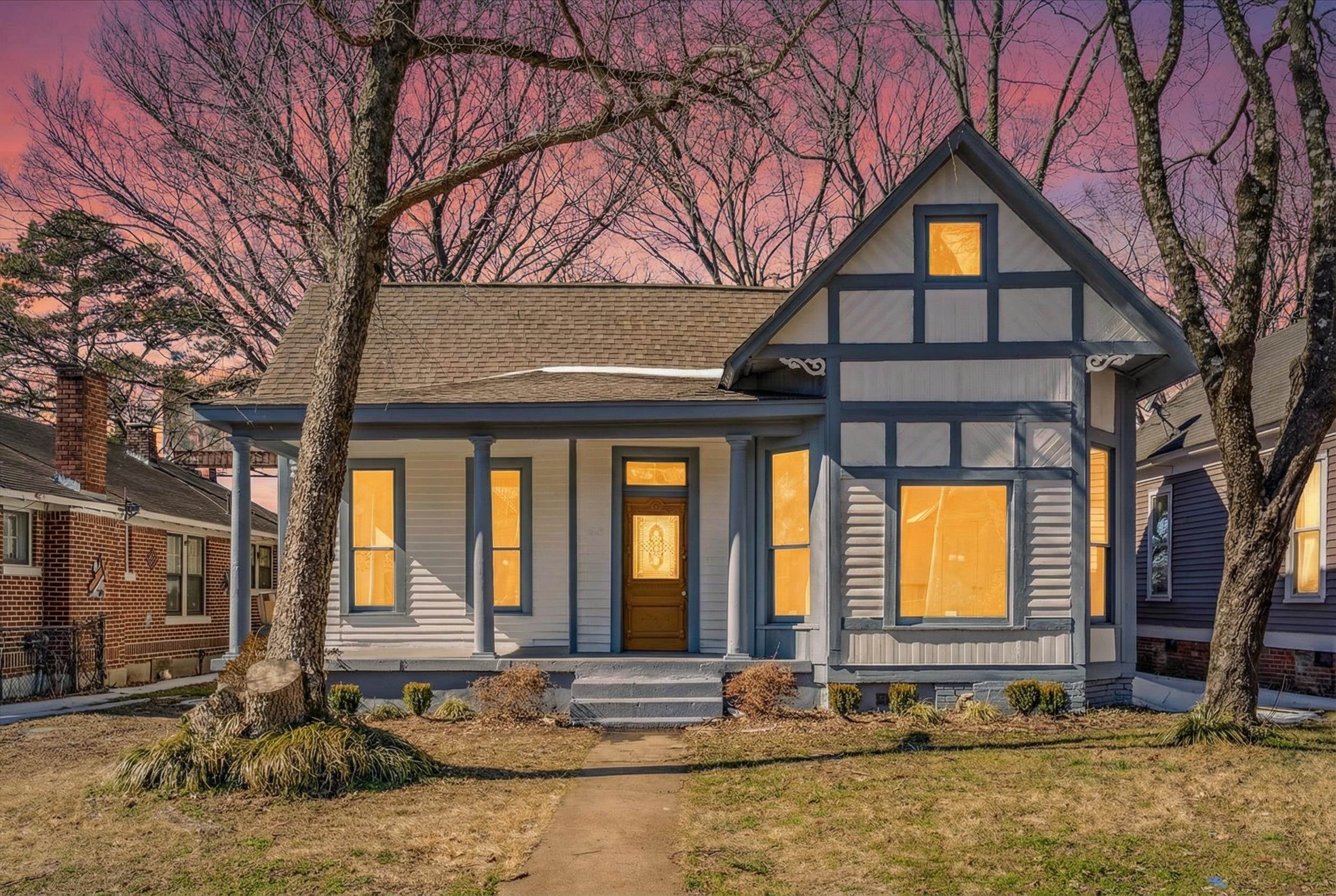 View of front facade with covered porch, a shingled roof, and a lawn