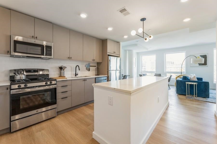 401 Jackson Street, Unit 507 Hoboken, NJ 07030 - Photo 11 of 29 a kitchen with stainless steel appliances granite countertop a stove top oven a sink dishwasher a refrigerator and a dining table with wooden floor
