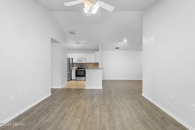 an empty room with wooden floor kitchen view and a window