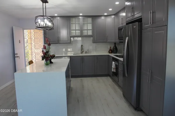 a kitchen with stainless steel appliances granite countertop a refrigerator a sink dishwasher a stove and a dining table with wooden floor