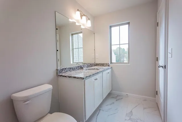 a bathroom with a granite countertop toilet a sink and a window
