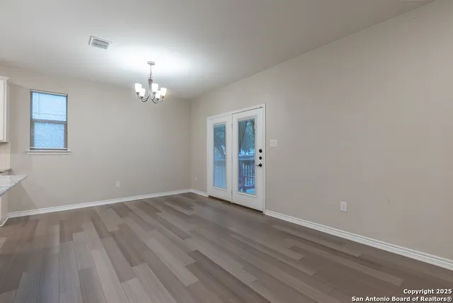 an empty room with wooden floor chandelier and windows