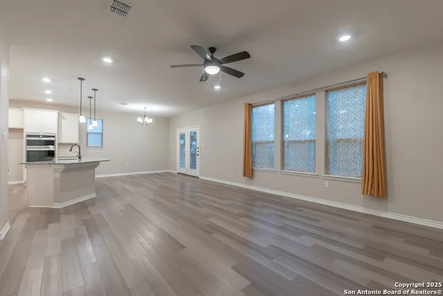 a view of an empty room with wooden floor and a kitchen