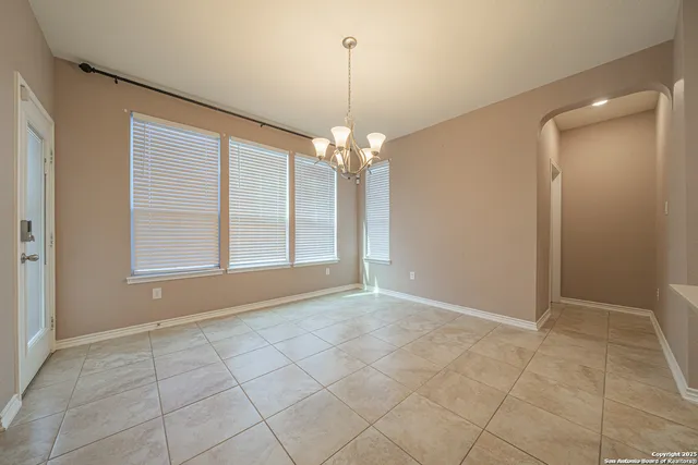 a view of an empty room with window and chandelier fan