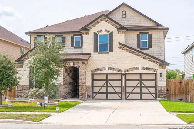 a view of a white house with a yard plants and large tree