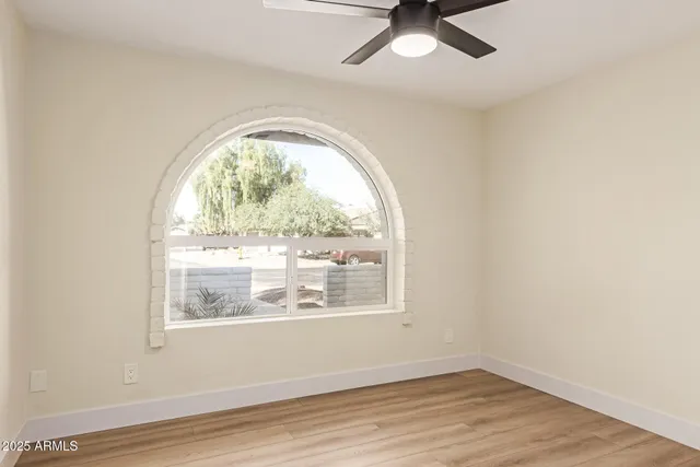 an empty room with wooden floor fan and windows