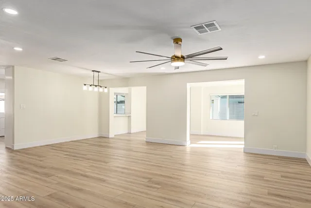 a view of an empty room with wooden floor and a ceiling fan