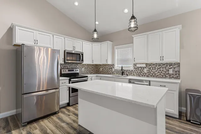 a kitchen with granite countertop a refrigerator oven a sink dishwasher and white cabinets with wooden floor