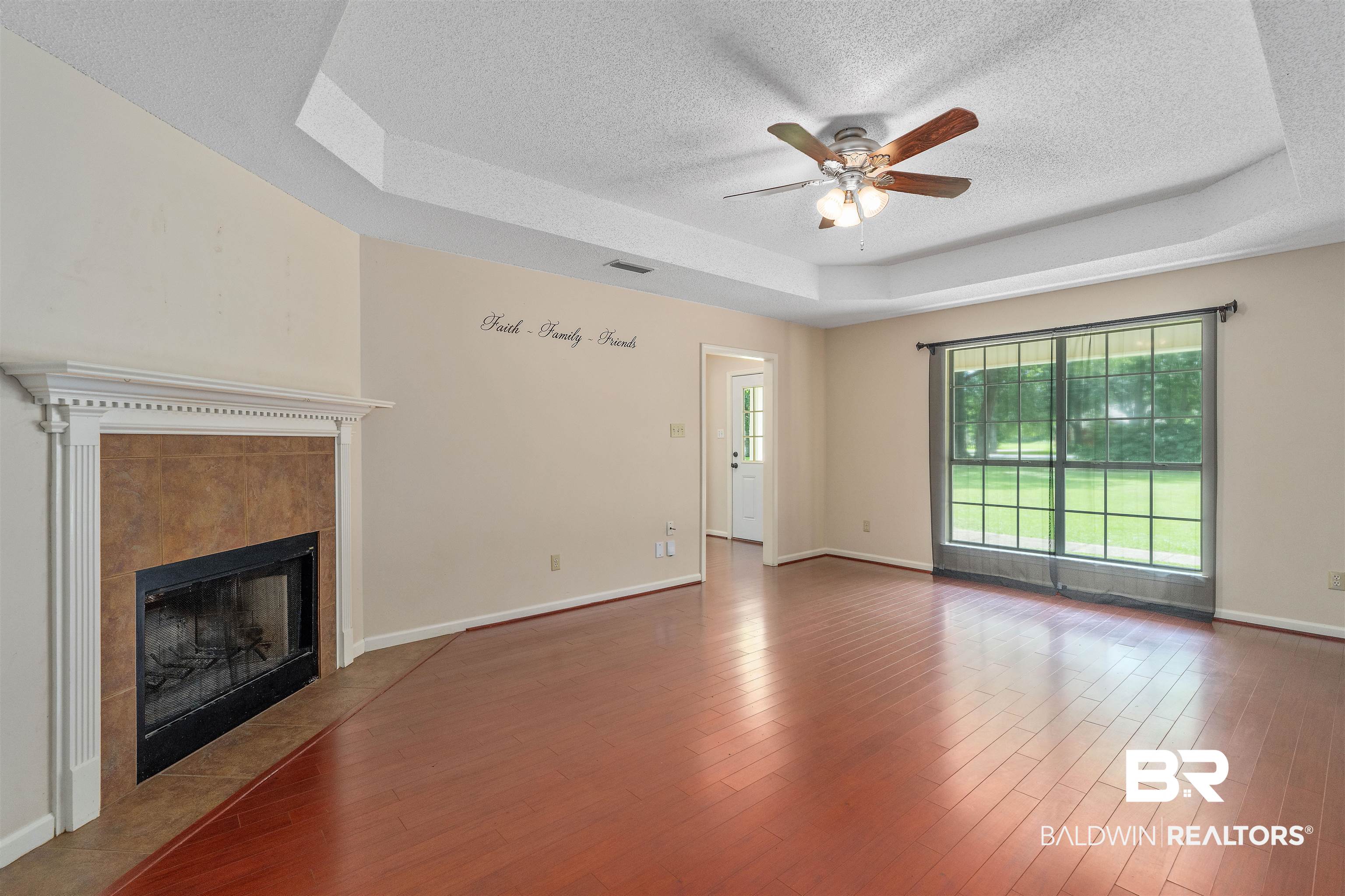 25779 Austin Road Daphne, AL 36526 - Photo 27 of 30 Unfurnished living room featuring a textured ceiling, a tray ceiling, ceiling fan, a tiled fireplace, and baseboards