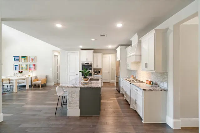 a kitchen with stainless steel appliances kitchen island granite countertop a stove a sink and white cabinets with wooden floor