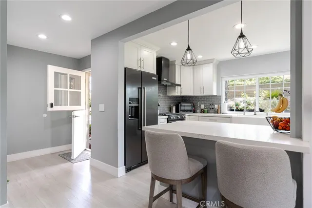 a kitchen with stainless steel appliances granite countertop a refrigerator a sink dishwasher a stove and a dining table with wooden floor