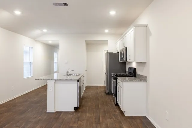 a kitchen with stainless steel appliances granite countertop a stove top oven a sink a refrigerator and white cabinets with wooden floor