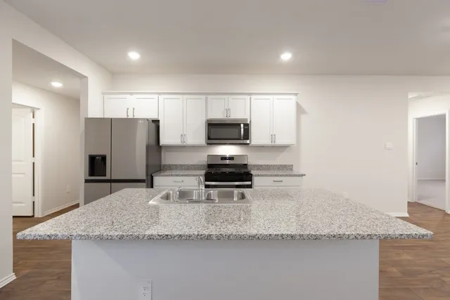 a kitchen with granite countertop a refrigerator a sink a stove a microwave and island