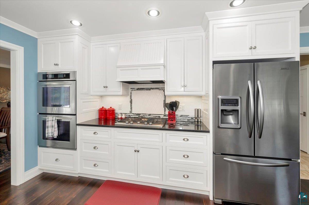 1323 South Ridge Road Duluth, MN 55804 - Photo 7 of 31 Kitchen featuring stainless steel appliances, premium range hood, backsplash, dark hardwood / wood-style floors, and white cabinetry