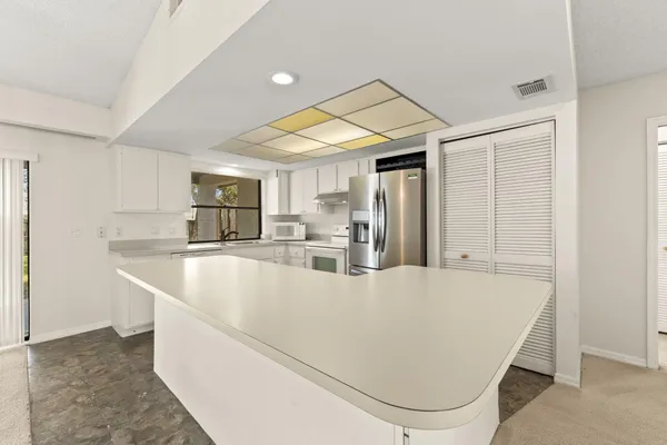 a large white kitchen with kitchen island a large window a counter space and stainless steel appliances