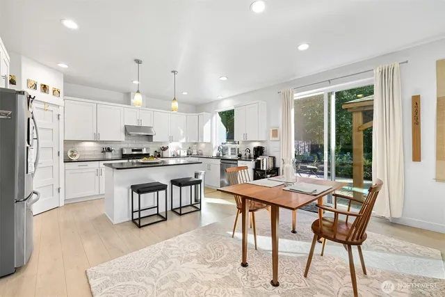 a kitchen with stainless steel appliances kitchen island granite countertop a refrigerator a stove a sink a dining table and chairs with wooden floor
