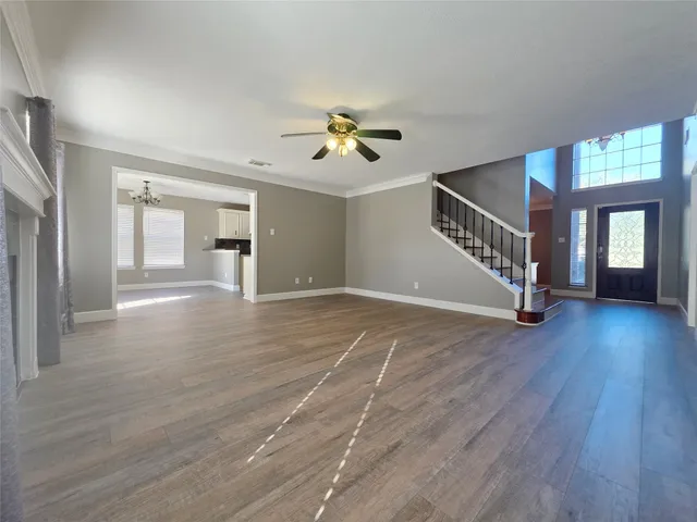 a view of an empty room with wooden floor and a ceiling fan