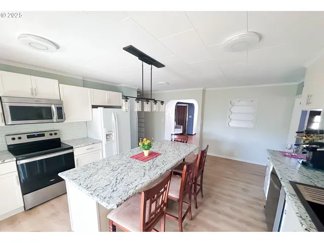 a kitchen with stainless steel appliances kitchen island granite countertop a table chairs in it and white cabinets