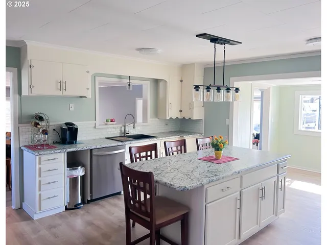 a kitchen with stainless steel appliances granite countertop a refrigerator a sink dishwasher a dining table and chairs with wooden floor