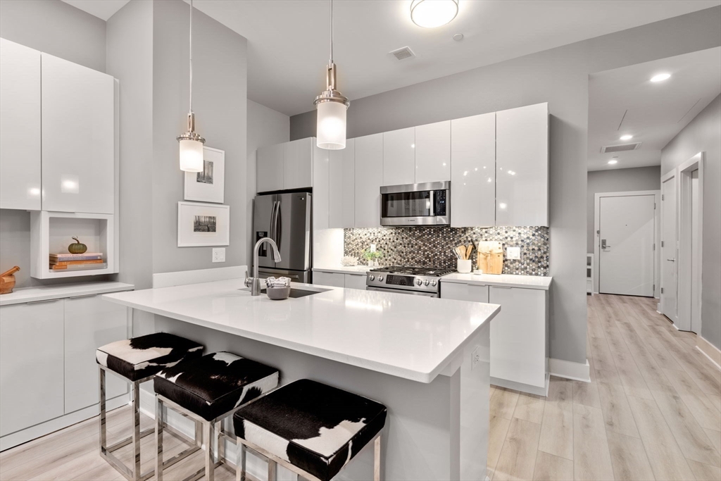 121-127 Portland Street, Unit 202 Boston, MA 02114 - Photo 3 of 25 a kitchen with kitchen island a stove a sink a refrigerator and chairs