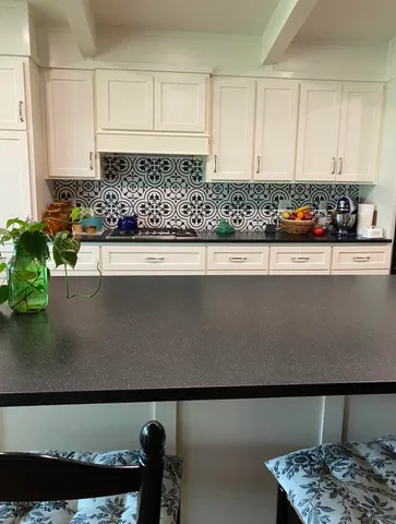 a view of kitchen island with stainless steel appliances granite countertop a sink a stove and white cabinets