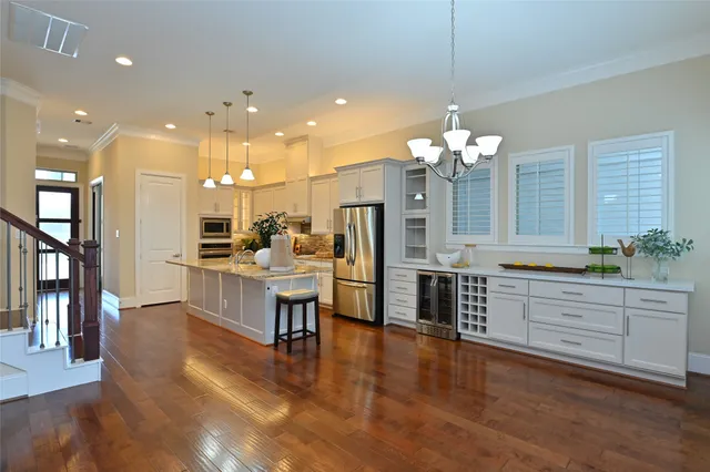 a large white kitchen with granite countertop a stove a sink a large island with chairs and wooden floor