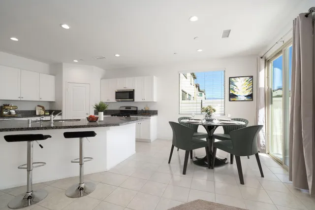 a kitchen with stainless steel appliances kitchen island granite countertop a dining table chairs and a refrigerator
