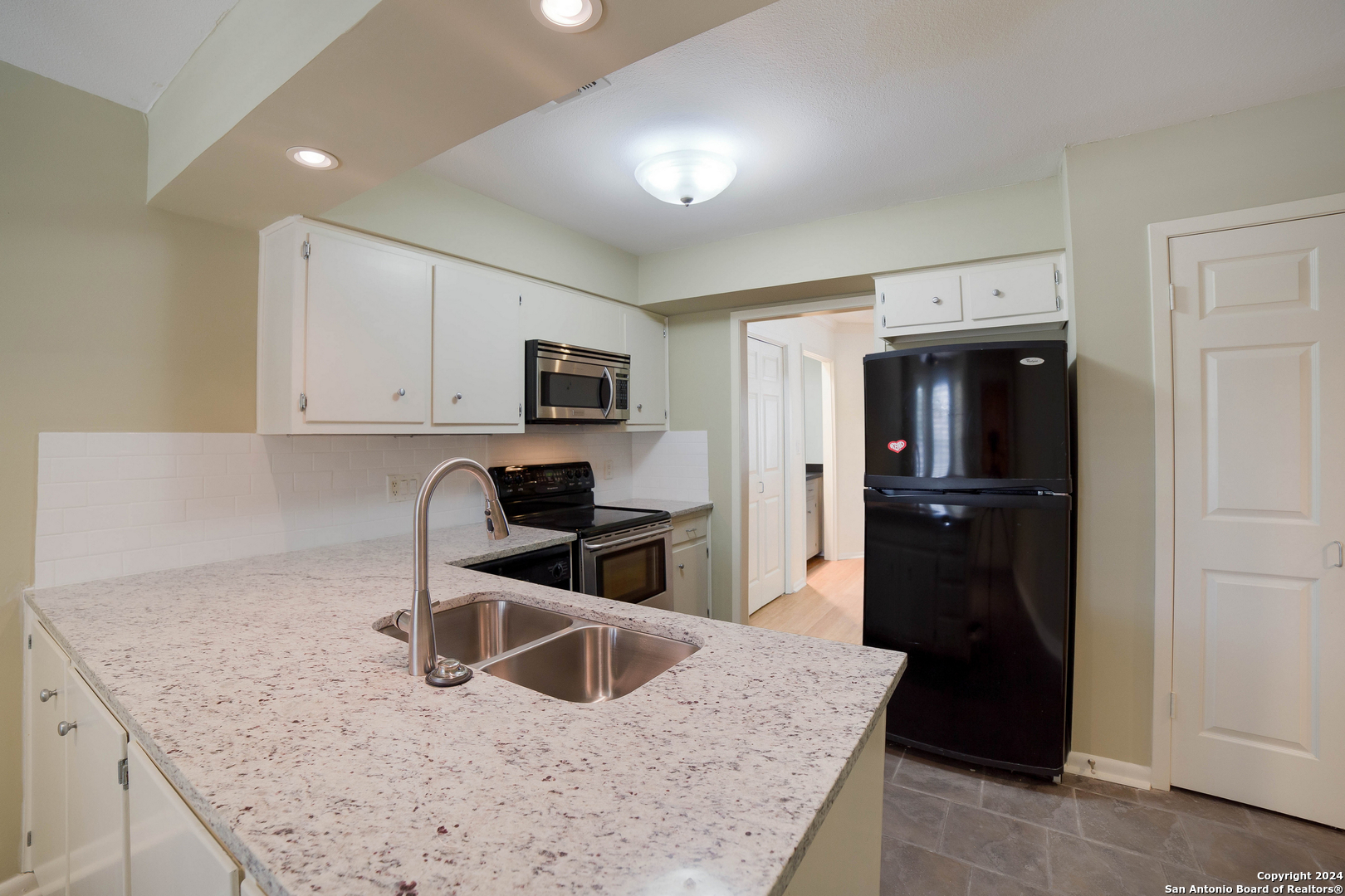 a kitchen with granite countertop a refrigerator a stove a sink a counter space and cabinets