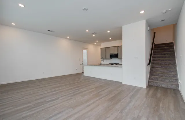 a view of an empty room with wooden floor and a kitchen