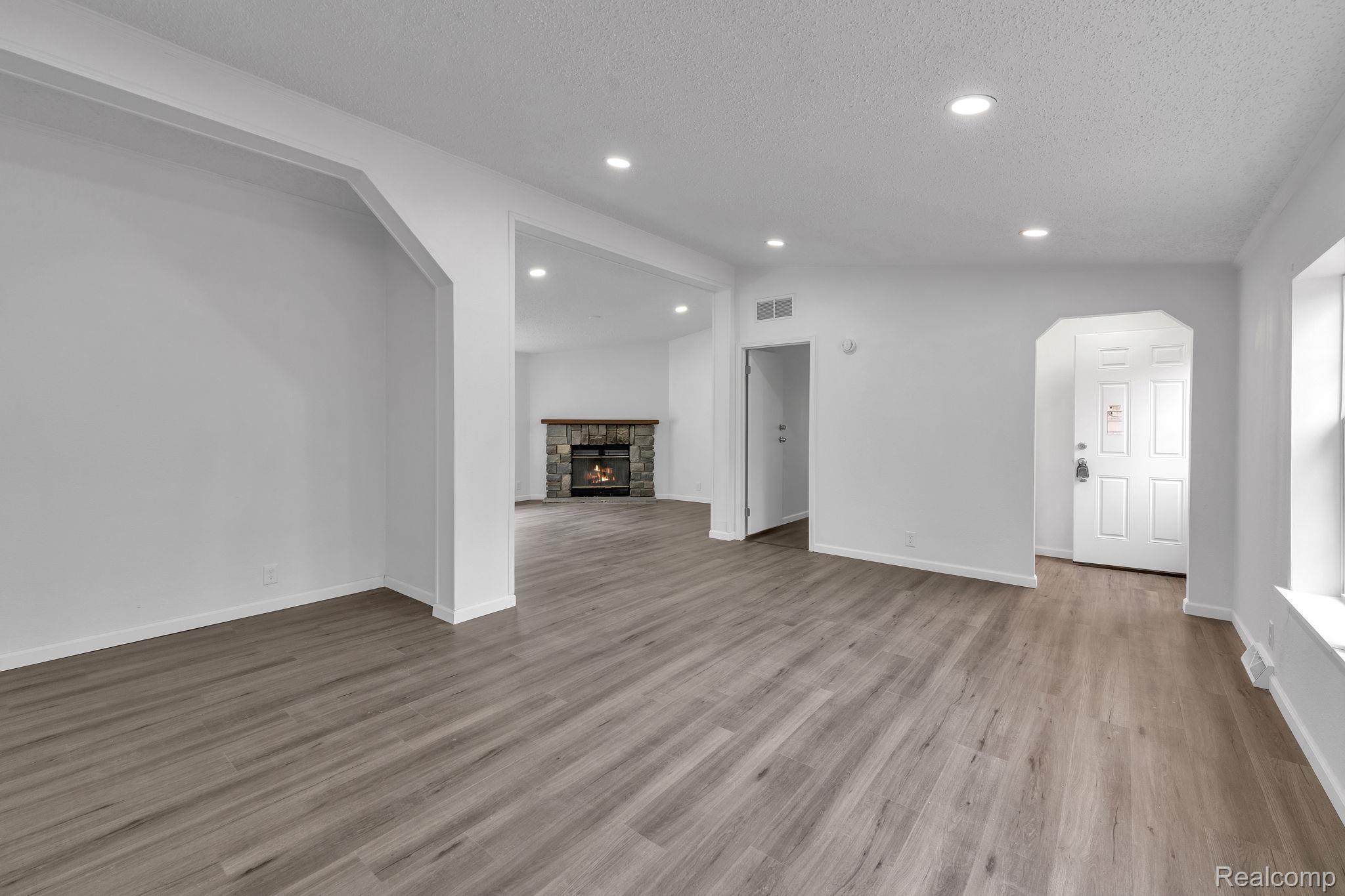 36085 Wick Road Romulus, MI 48174 - Photo 21 of 43 Unfurnished living room with arched walkways, a stone fireplace, recessed lighting, and wood finished floors