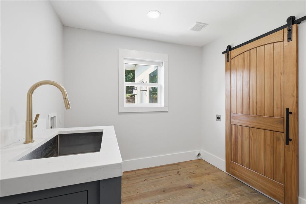 4310 Forest Bend Road Dallas, TX 75244 - Photo 24 of 40 Laundry area featuring a wood-finish barn door, light wood-finish flooring, and a window with white trim