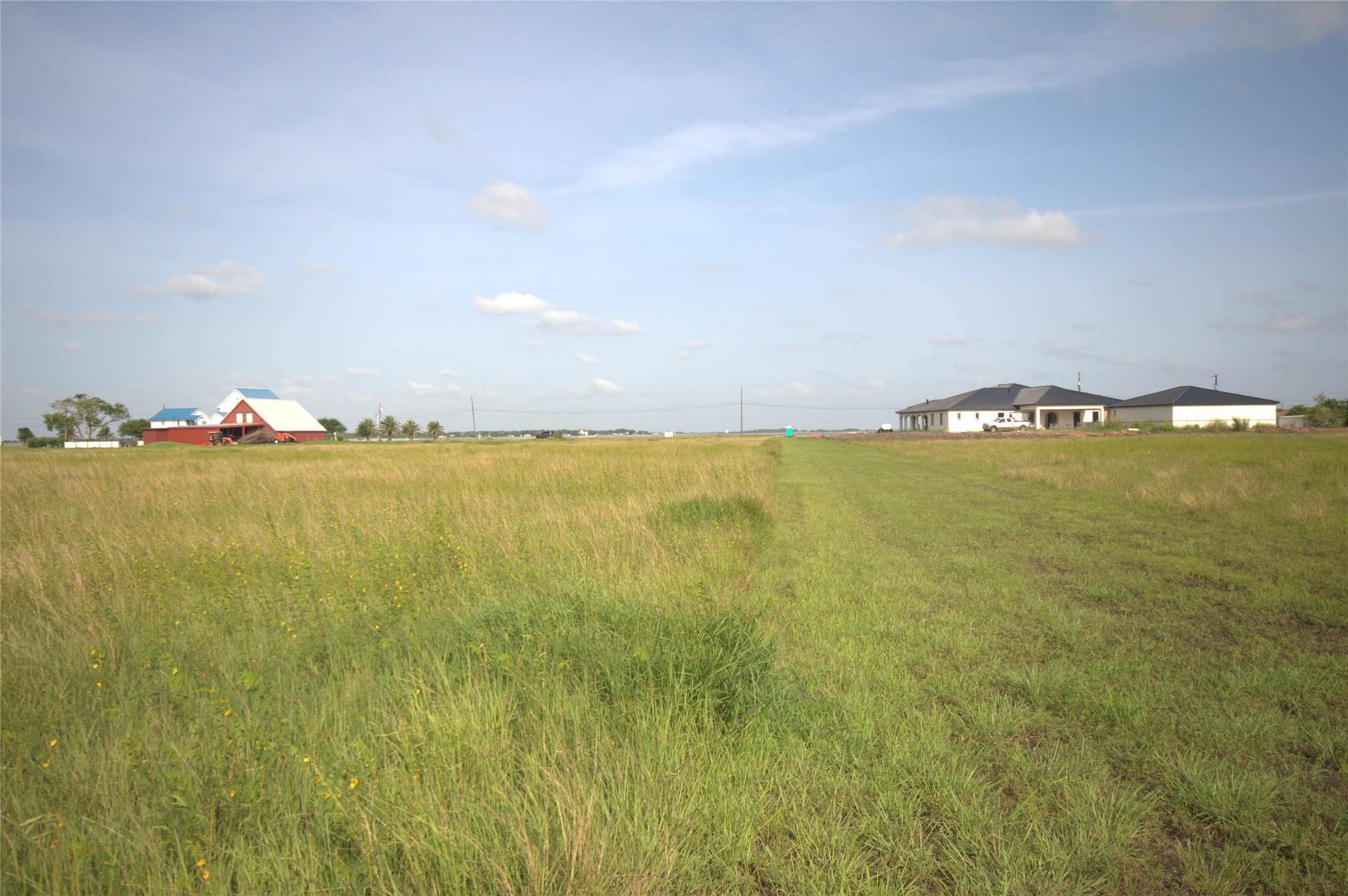 305 Bayshore Road Palacios, TX 77465 - Photo 7 of 25 A vast, open field offers a tranquil setting with distant residential structures under a clear sky.