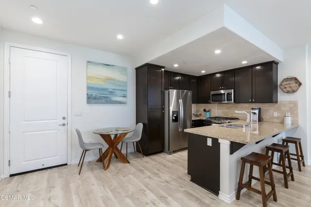 a kitchen with stainless steel appliances kitchen island granite countertop a refrigerator a stove a sink a dining table and chairs with wooden floor