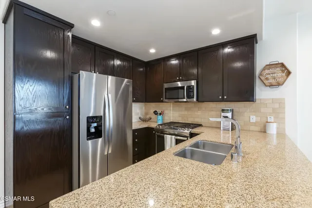a kitchen with granite countertop stainless steel appliances a refrigerator a stove a sink and a counter top space