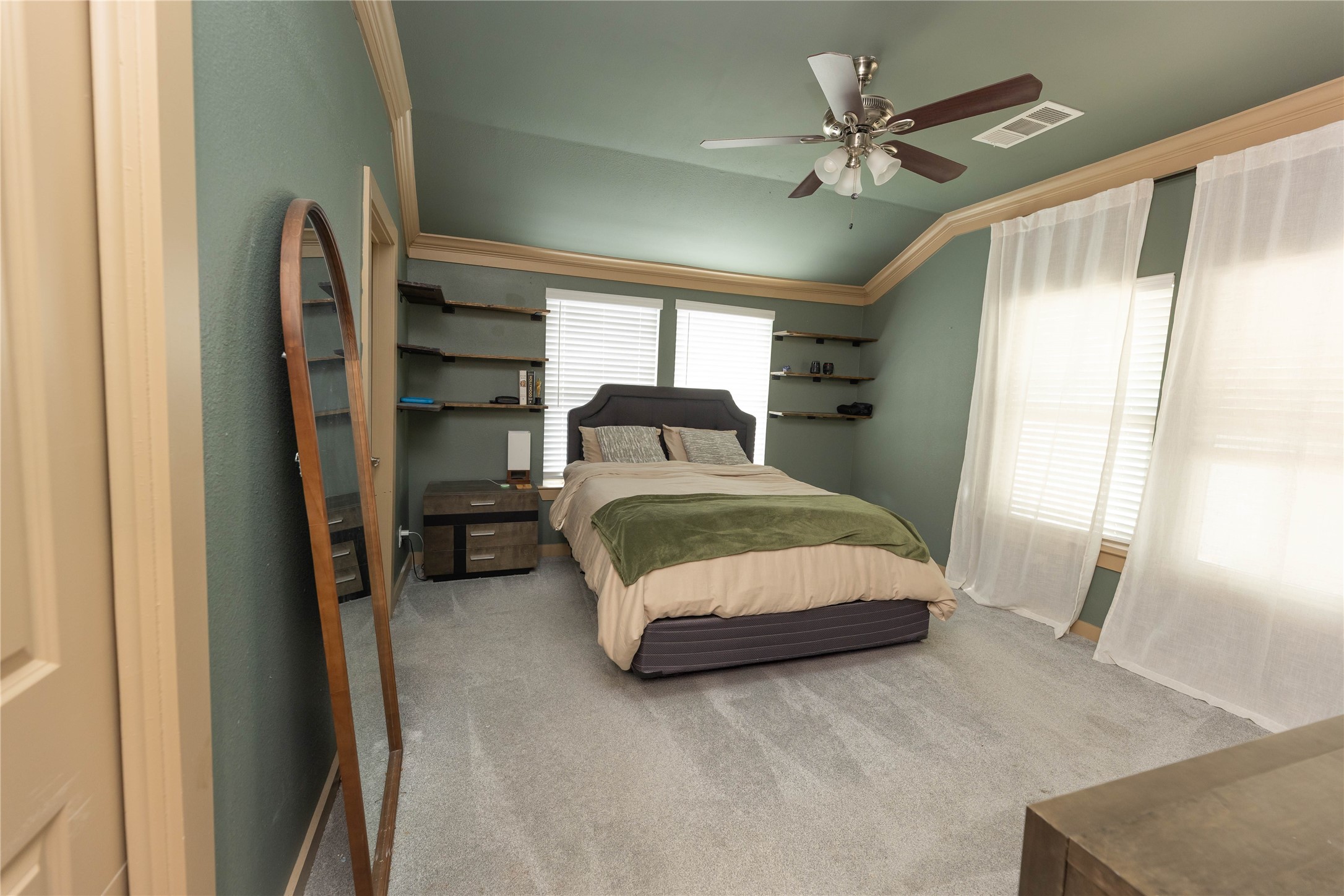 8007 Capitol Street Houston, TX 77012 - Photo 15 of 25 This bedroom features soft green walls with crown molding, a ceiling fan, and large windows with sheer curtains for ample natural light. It includes wall shelves for storage, offering a comfortable and stylish space.