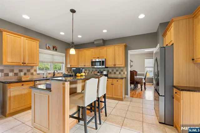a kitchen with stainless steel appliances kitchen island granite countertop a refrigerator a stove a sink a dining table and chairs with wooden floor