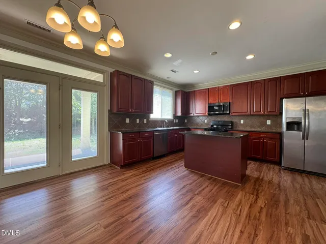 a kitchen with stainless steel appliances granite countertop wooden cabinets a refrigerator a stove a sink and dishwasher with wooden floor