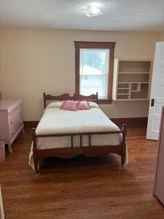 a bedroom with a bed chair and wooden floor