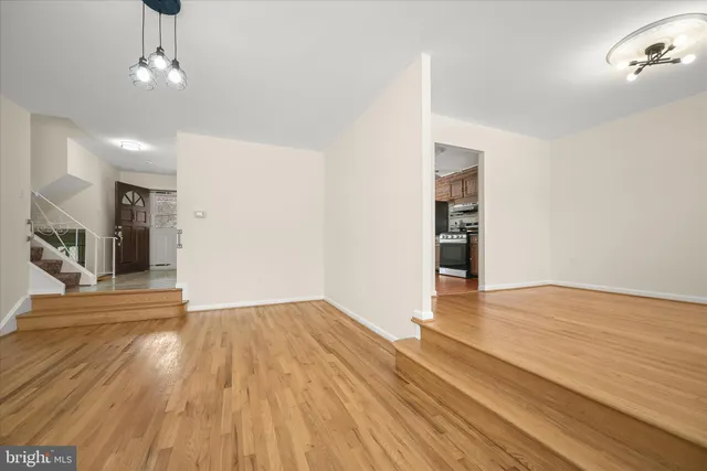 a view of an empty room with wooden floor and a kitchen