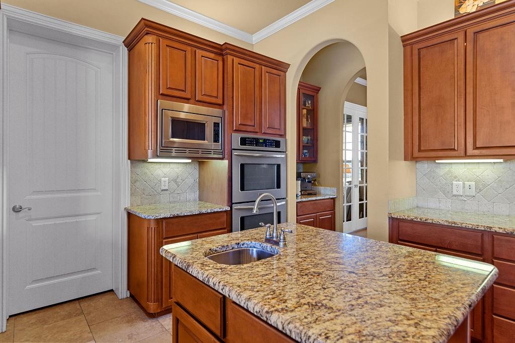 117 Citation Drive Cresson, TX 76035 - Photo 17 of 40 Kitchen featuring decorative backsplash, arched walkways, appliances with stainless steel finishes, crown molding, and light stone counters