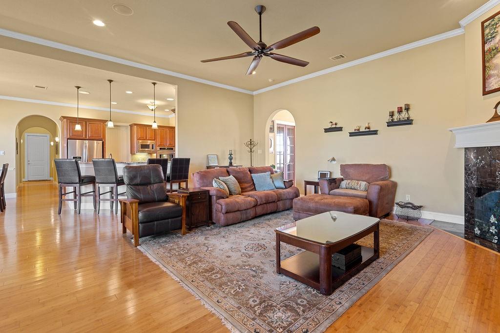 117 Citation Drive Cresson, TX 76035 - Photo 9 of 40 Living area with arched walkways, crown molding, light wood finished floors, a ceiling fan, and a premium fireplace