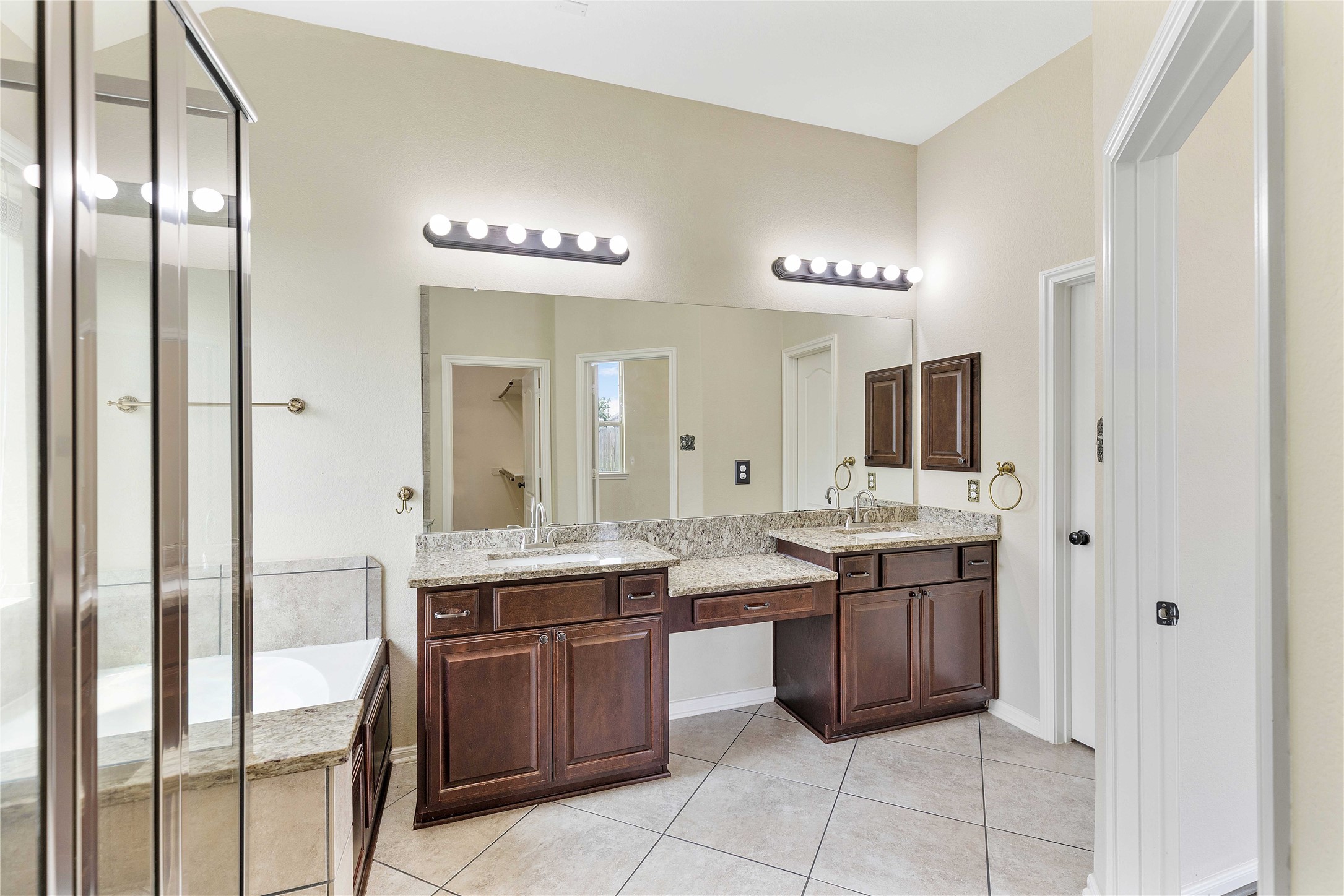 17206 Upper Ridge Lane Humble, TX 77346 - Photo 18 of 50 Primary bathroom features dual sinks with granite countertops, dark wood cabinetry, a large mirror with modern lighting, and a combination shower and bathtub. The neutral tile flooring and walls create a bright and inviting space.