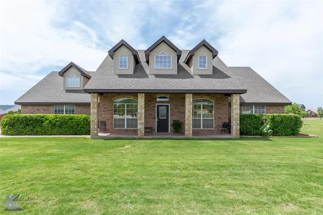 a view of a brick house with a big yard and large trees