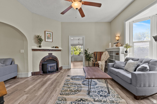 148 South 300 East Logan, UT 84321 - Photo 3 of 29 Living area featuring a brick fireplace with a wood-burning insert, wood-finish flooring, a ceiling fan with integrated lighting, and a prominent bay window