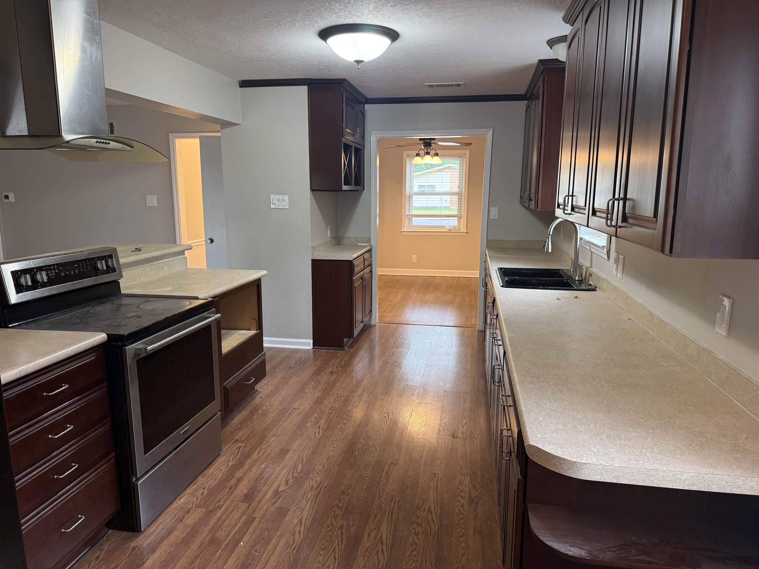 1918 Cherry Road Memphis, TN 38117 - Photo 3 of 26 Kitchen featuring wood-finish flooring, dark wood cabinetry, light-toned countertops, and stainless steel appliances including a range with an overhead vent hood