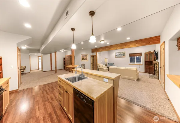 a view of a kitchen with kitchen island a stove a sink a oven and a dining table with wooden floor