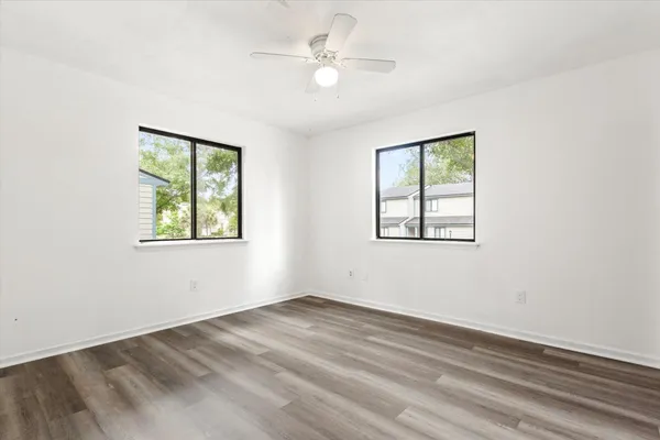 an empty room with wooden floor ceiling fan and windows