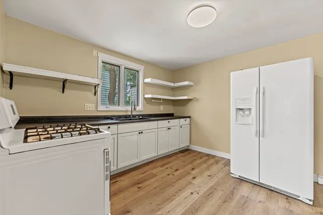 a kitchen with granite countertop a refrigerator a sink and white cabinets